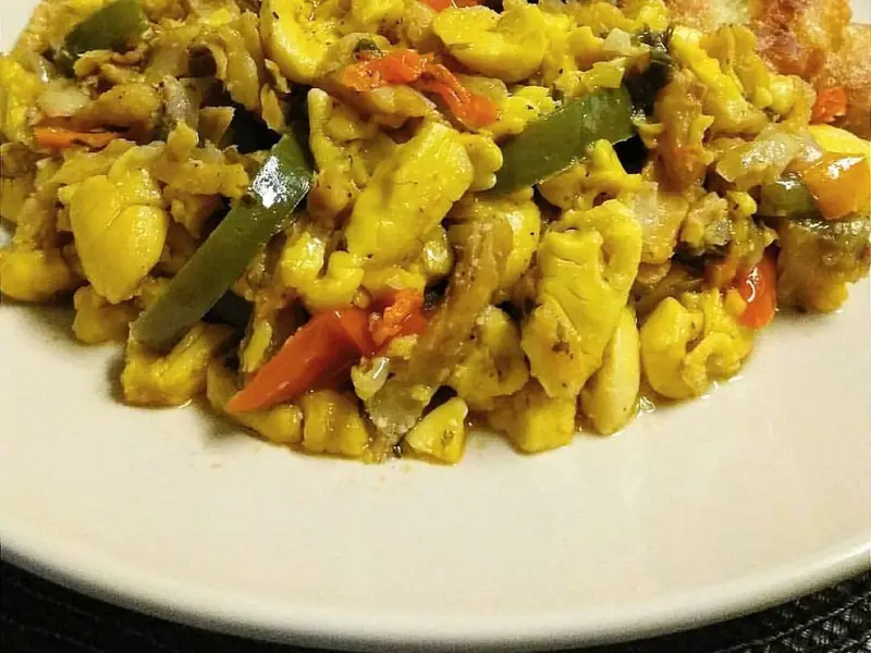 Ackee and saltfish with green and red peppers and tomato on a white plate, served with three golden fried fritters or dumplings