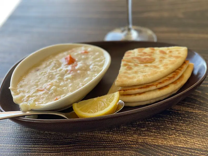 Creamy rice soup with carrot pieces in a white oval bowl, served with folded flatbread wedges, a lemon wedge and a spoon on a dark plate