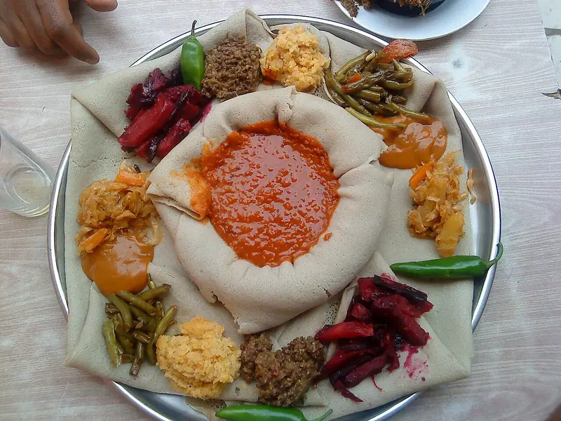 Metal tepside injera; ortada kırmızı mercimek yemeği, etrafında pancar, taze fasulye, lahana, sarı kuru bezelye, yeşil mercimek ve yeşil acı biberler