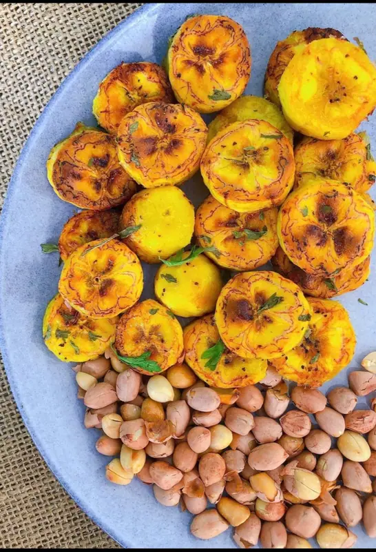 Runde skiver af gyldent ristet plantain med ristede pletter og hakkede krydderurter på en blå tallerken med flåede peanuts ved siden af.