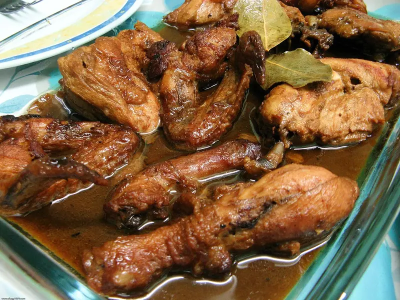 Brunede kyllingbiter med bein, blant annet kyllinglår, braisert i en mørk, blank saus med laurbærblad i en ildfast glassform.