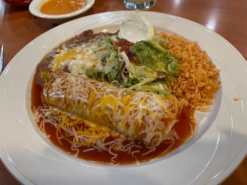 A large tortilla smothered in red sauce and melted cheese, with refried beans, Mexican rice, shredded lettuce, guacamole and sour cream.