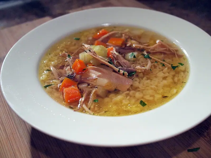 Tær gullin kjúklingasúpa með litlu hringpasta, rifnum kjúklingi, smátt skornum gulrótum og selleríi, stráð steinselju í hvítri skál