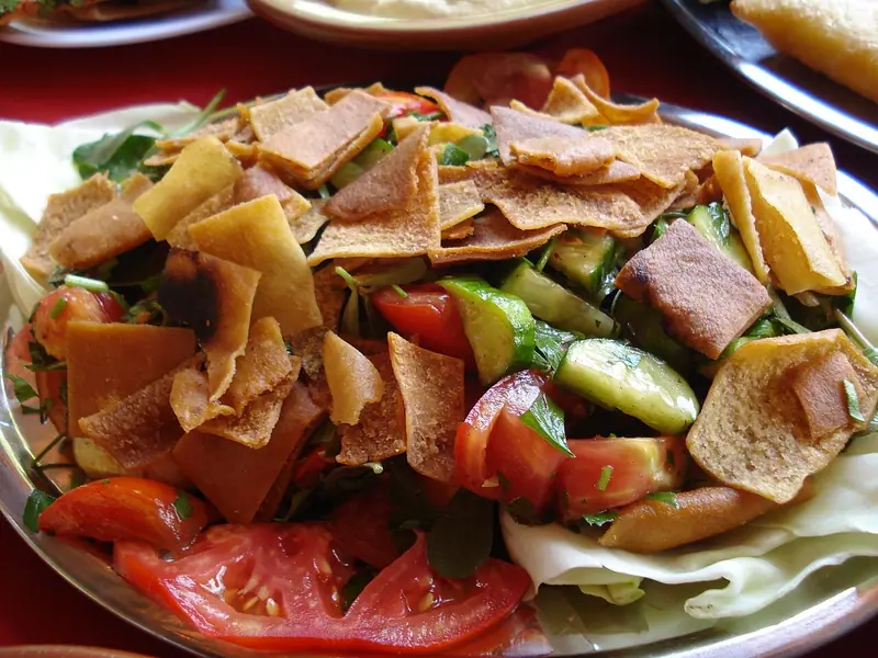 Fattoush-salat med tomat, agurk og krydderurter toppet med sprøde gyldne pitachips på et metalfad beklædt med kålblade