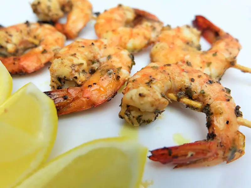 Crevettes grillées avec la queue, sur des brochettes en bois, enrobées d'herbes et d'épices, dans une assiette blanche avec des quartiers de citron