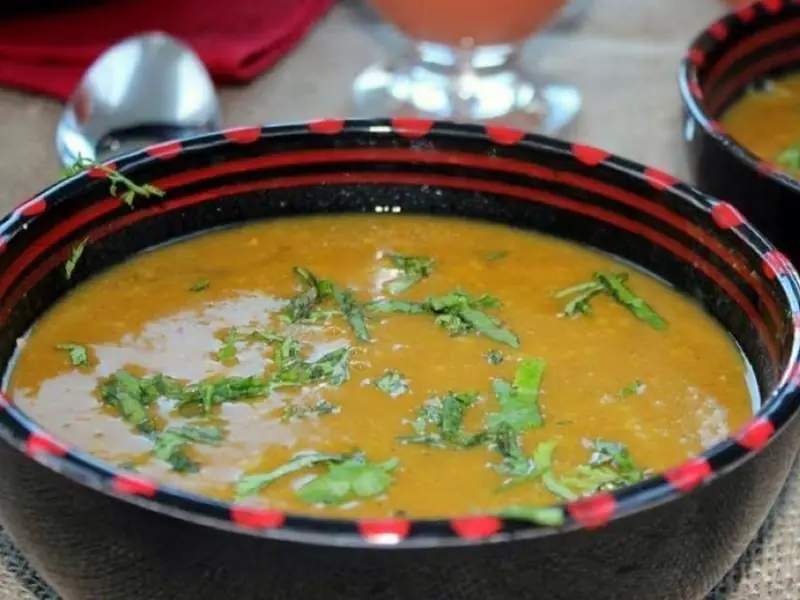 Zwei schwarze Schalen mit rot gepunktetem Rand, gefüllt mit sämiger orange-brauner Suppe und bestreut mit gehacktem Koriander, auf einer Tischdecke aus Jute.