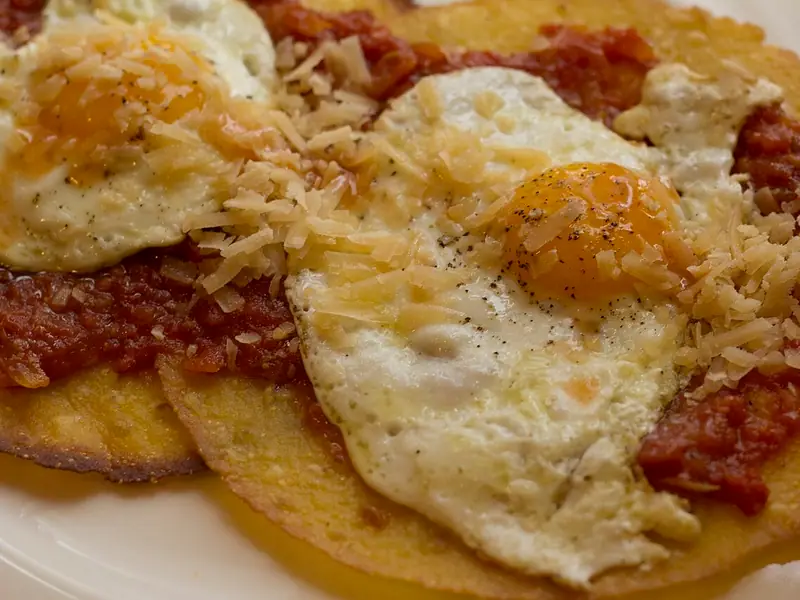 Spæld egg á stökkum, gullnum tortillum með grófri rauðri tómatsalsa, toppuð með rifnum hörðum osti og svörtum pipar á hvítum diski