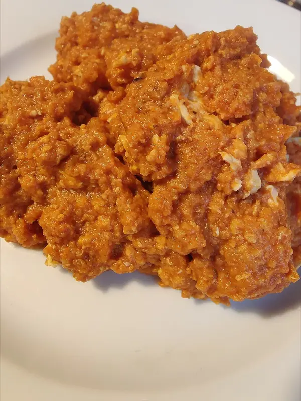 Ein Häufchen orangerotes Püree aus Auberginen und Tomaten mit Rührei-Stückchen auf einem weißen Teller.