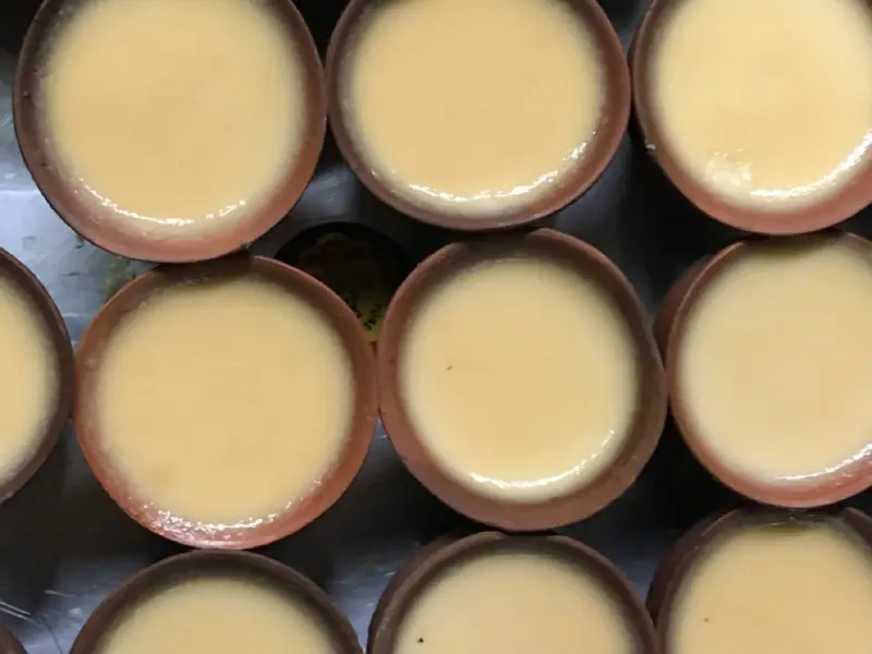 Overhead view of rows of small terracotta clay pots filled with smooth, pale creamy-yellow set yogurt.
