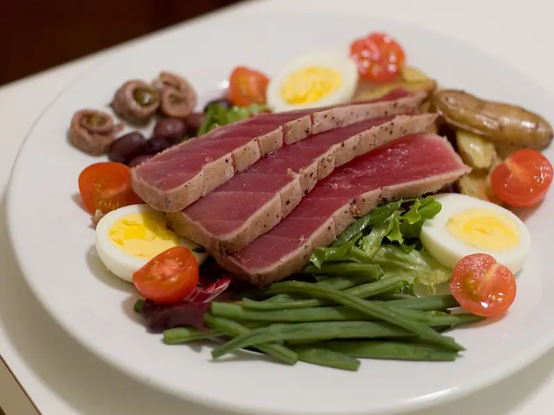 Sliced seared tuna steak on greens with halved boiled eggs, cherry tomatoes, green beans, roasted fingerling potatoes, olives and anchovies