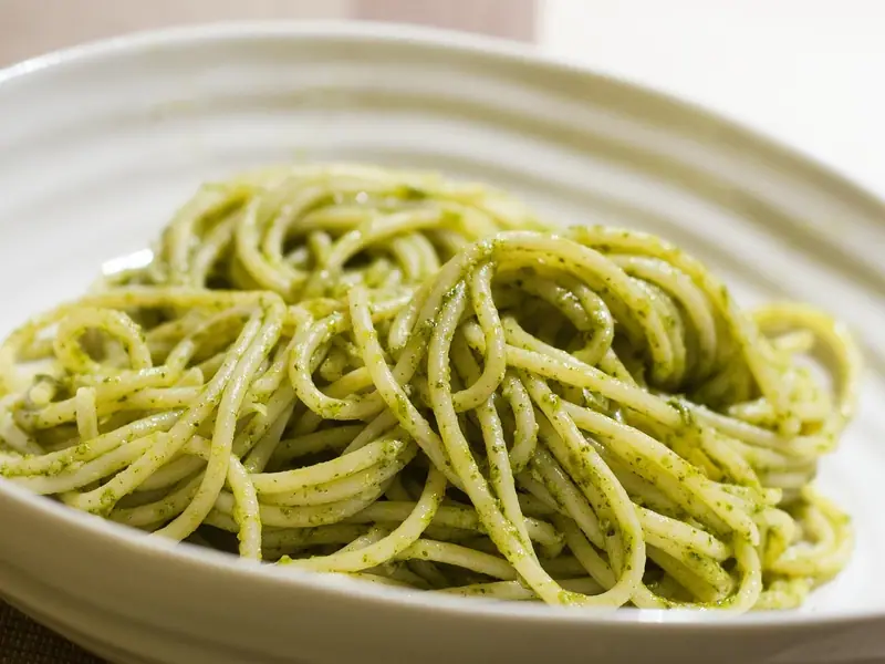 Spaghetti vendt i grøn basilikumpesto, snoet op i en lille top i en hvid riflet skål.