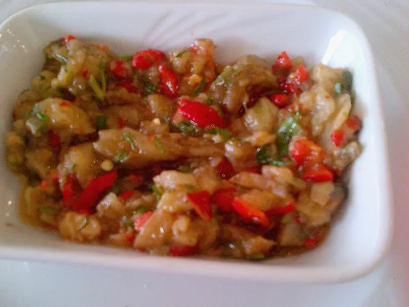 다진 구운 가지에 빨간 파프리카 조각과 신선한 허브를 더해 오일로 윤기 나게 버무린 샐러드를 흰색 사각 그릇에 담은 모습.