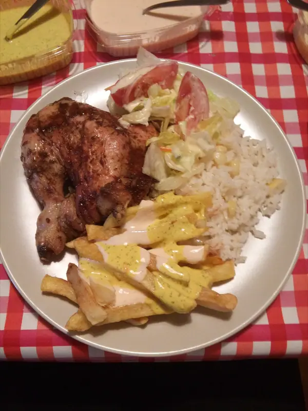 Beyaz tabakta pilav, marul ve domates salatası ve üzerine sarı ve beyaz sos gezdirilmiş patates kızartmasıyla servis edilen fırınlanmış tavuk but.
