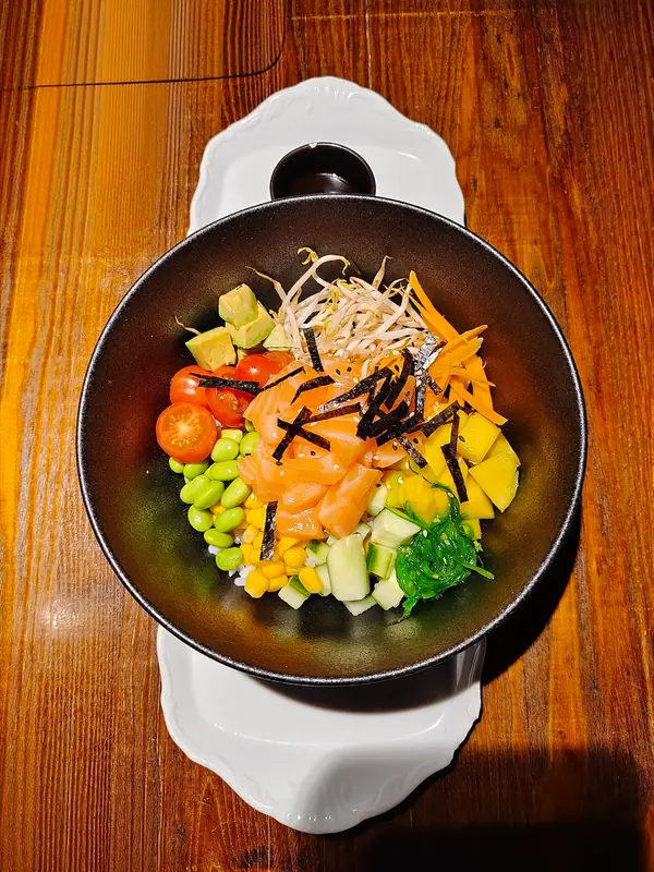 Poke bowl de salmón con arroz blanco, edamame, maíz, tomates cherry, aguacate, mango, ensalada de algas, brotes de soja, zanahoria y tiras de nori