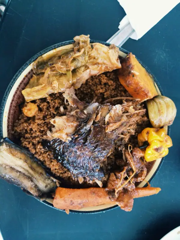 Pogled od zgoraj na lomljeni riž z zapečeno ribo, dušenim zeljem, jajčevcem, korenjem, sladkim krompirjem in rumenim čilijem Scotch bonnet