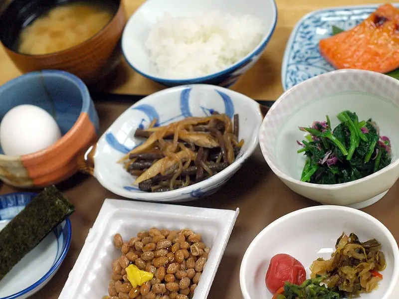 Tavă cu mic dejun japonez: orez, supă miso, somon la grătar, un ou, natto cu muștar, nori, verdețuri, legume fierte înăbușit și murături