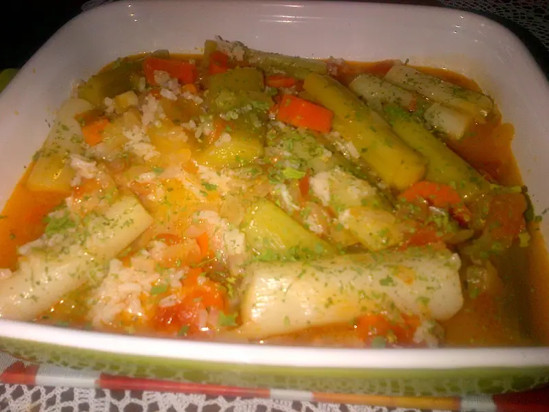 Braised leek pieces with carrot, tomato and rice in an orange broth, sprinkled with green herbs, in a white square baking dish.